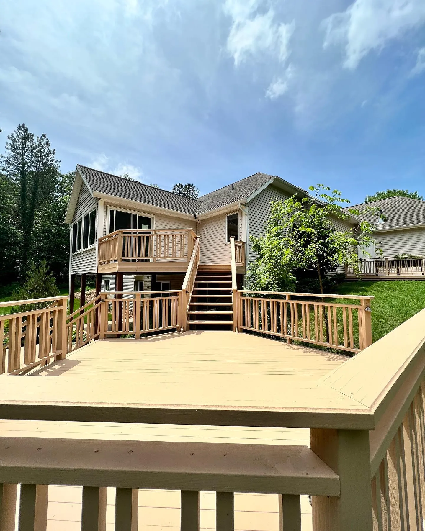 A light-colored wooden deck with stairs leads up to the back entrance of a beige house with a porch in Caledonia, Michigan, surrounded by greenery under a partly cloudy sky—perfect for relaxing after residential painting projects.