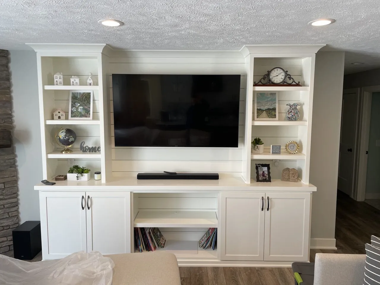 Wall-mounted flat screen TV with white built-in shelves and cabinets, displaying decor items, books, and a soundbar below the TV—perfectly complementing a fresh interior painting project in Ada Michigan.