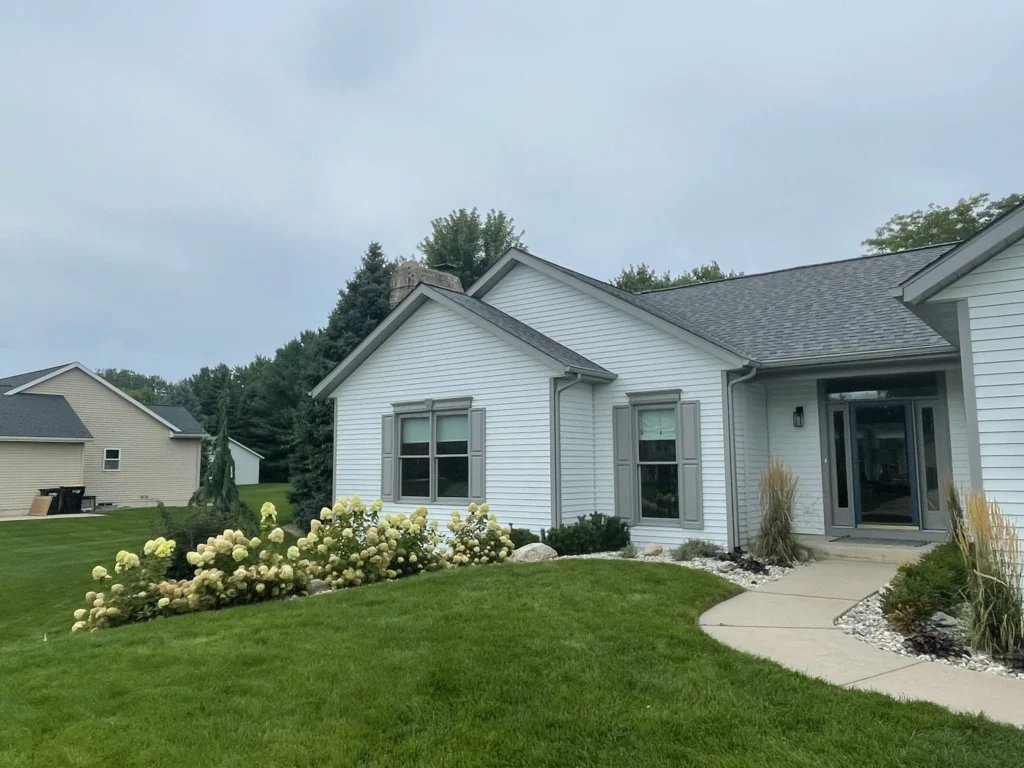 Single-story white house with gray roof in Caledonia, Michigan, bordered by green lawn, blooming shrubs, and a curved concrete walkway leading to the front door—ideal for those seeking expert residential painting or interior painting services.
