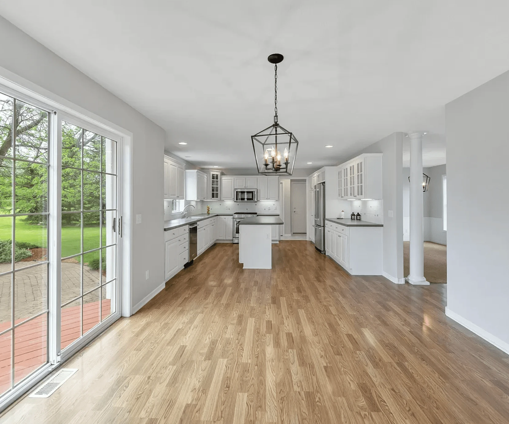 Bright, modern kitchen with freshly painted white cabinets, stainless steel appliances, wood-style flooring, and a large glass sliding door overlooking a green backyard in Caledonia, Michigan.