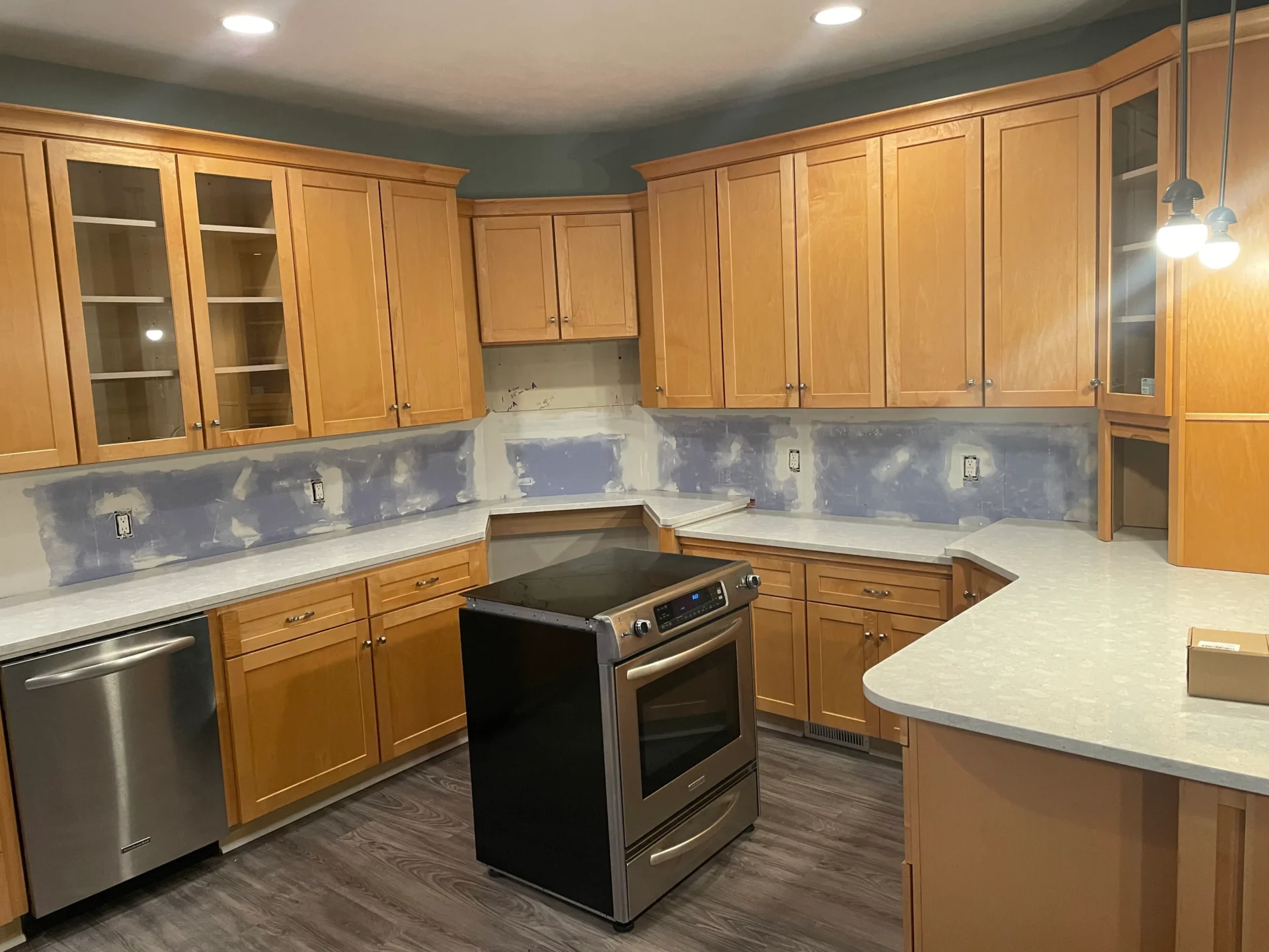 Kitchen with light wood cabinets, a stainless steel dishwasher and stove, white countertops, and unfinished wall backsplash ready for tiling. - Jeff Bryant Painting