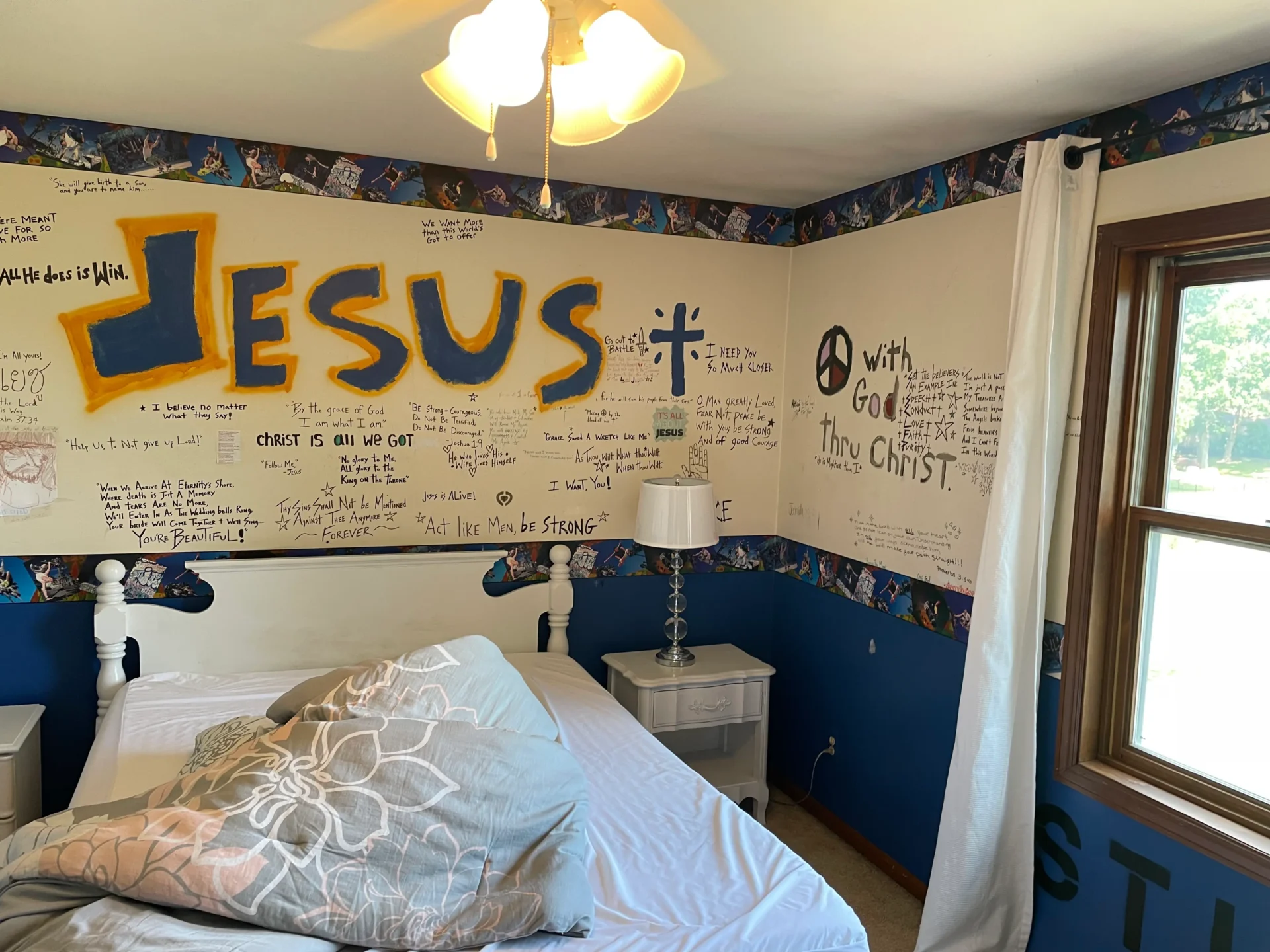 A bedroom with two twin beds, white bedding, and handwritten religious messages and decorations on the wall, including "JESUS" in large yellow letters. - Jeff Bryant Painting
