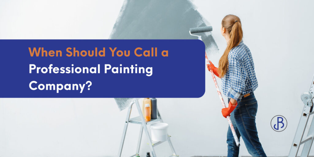 A person paints a white wall with gray paint using a roller. Text reads, “When Should You Call a Painting Company?” A ladder and paint supplies are nearby, highlighting the benefits of hiring professionals for your next project.