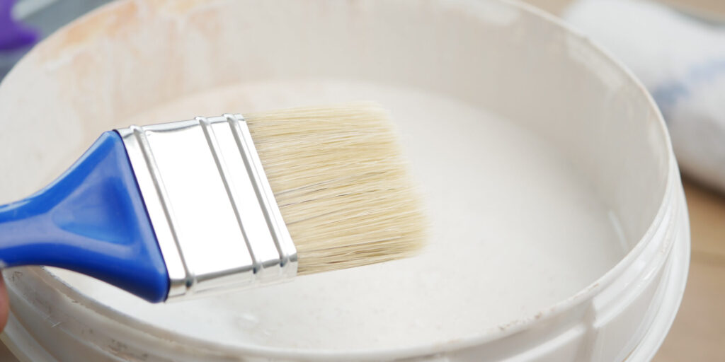 Blue paintbrush resting on a white paint bucket, symbolizing professional wall painting with a smooth, flat finish.