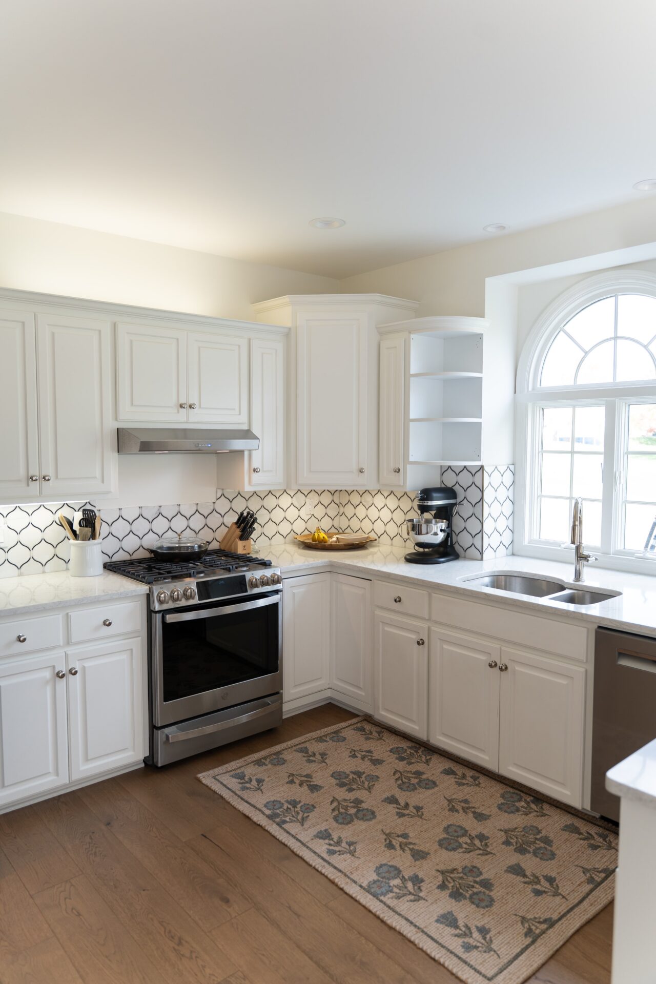 Modern kitchen with white cabinets, stainless steel appliances, a patterned rug, and a large arched window letting in natural light—expert interior painting Alto Michigan enhances the fresh, welcoming atmosphere. - Jeff Bryant Painting